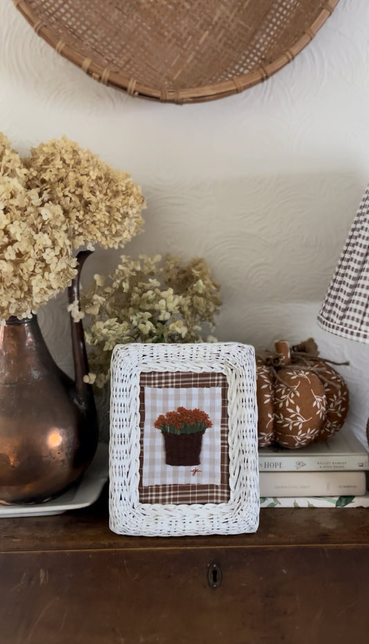 Burnt Orange Mum in Basket Embroidery Stitched on a Rust-Colored Plaid Fabric and Framed in a White Wicker Frame